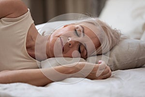 Calm serene older woman sleeping alone in bed, closeup view