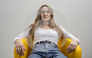 Calm serious arrogant business woman or student in casual cloth sitting in yellow office chair relaxing isolated on grey