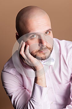 Calm serious attractive bald bearded man sitting keeps hand on his face, looking at camera.