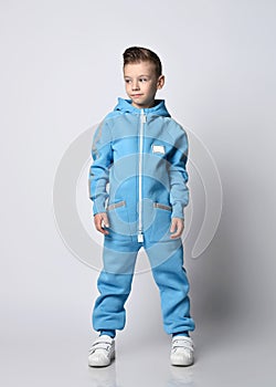Calm, smart kid boy in blue jumpsuit with zipper and reflective stripes stands looking aside at copy space