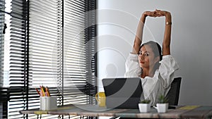 A calm smiling businesswoman is relaxing at office chair and stretching raising hands up.