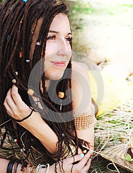 Calm smiling girl portrait with dreadlocks, resting on the dry grass in park