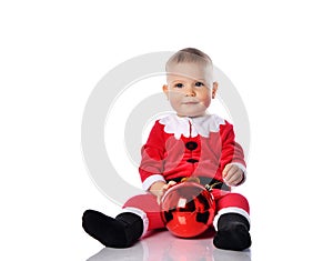 Calm and smiling little child boy toddler in santa claus costume is holding christmas tree red ball fir decoration