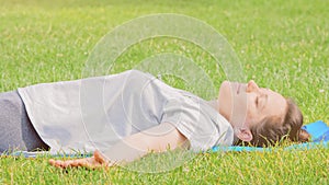 Calm smiling woman resting on green grass, raised her hands up