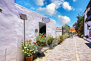 Calm street in rural village, bright white houses, row colorful flower pots, blue summer sky - Betancuria, Fuerteventura