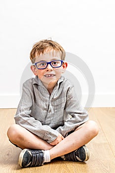 Calm studious child with eyeglasses and a missing tooth sitting photo
