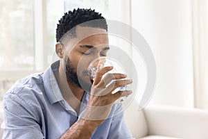 Calm thirsty young African man drinking fresh clear water