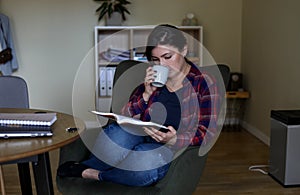 Calm, tired and pensive mature woman drinking tea and reading book at home. Education study. Training for new occupation