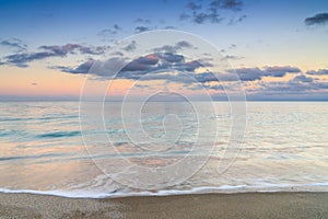 Calm turquoise ocean water under a olorful sunset sky with calm waves on the sandy shore