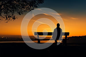 Calm twilight, Silhouetted man sits on bench during peaceful sunset