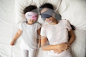 Calm Vietnamese mother and small daughter daydream in bed