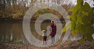 Calm weekend at nature, woman and her little son are admiring forest lake at autumn day, walking and resting in woodland