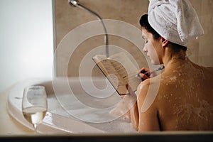 Calm woman having a relaxing bath at home.Spa self care night.Inspired creative person writing gratitude diary/journal.Resolution