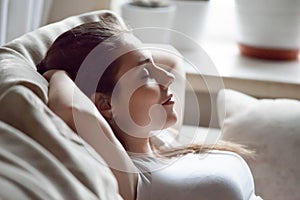 Calm woman relaxing on sofa hands over head