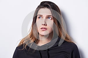 Calm woman standing by white wall looking to side