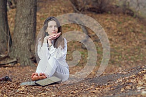 Calm woman in white clothes is resting after standing on sharp nails. A young yogi girl sits on the ground in the autumn