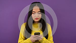 Calm young asian woman in bright yellow sweater typing a text message on the smartphone. 4K
