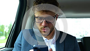 Calm young businessman sitting on back seat of car while using mobile phone to communicate. Business, trip, transport