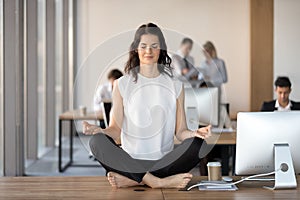 Calm young businesswoman doing yoga exercise at work desk