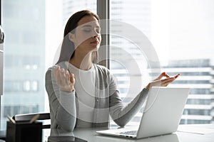 Young woman employee meditating practicing yoga at workplace