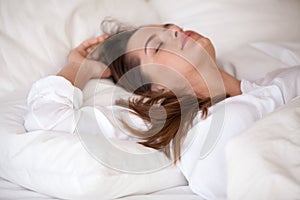 Calm young female sleeping in cozy white bed relaxing