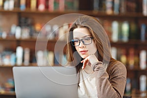 Calm young girl in eyeglasses working on laptop in cafe