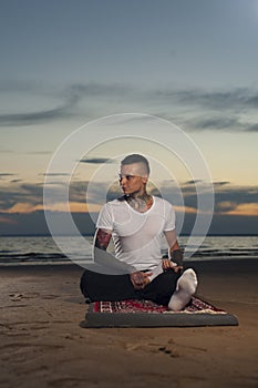 Calm young man doing yoga on the beach at sunset