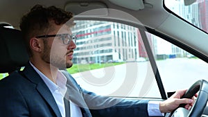 Calm young man in glasses driving along the street on the car and looking at the road. Side view. Transport, business