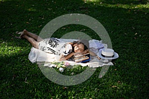 Calm young woman falling asleep on a stack of books, enjoys nature and sunny weather