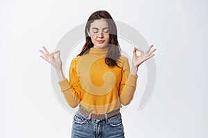 Calm young woman meditating and relaxing, standing in peace with patient face expression, holding hands in zen om