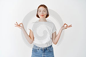 Calm young woman meditating, smiling with eyes closed and zen gesture, practice yoga to relax, resting mind, standing on