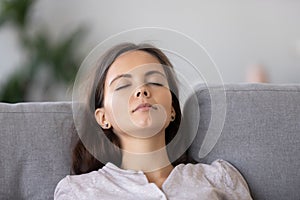 Calm young woman relaxing on comfortable sofa with closed eyes close up