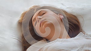 Calm young woman sleeping well in comfortable cozy bed on white soft pillows linen and waking up in the morning,insomnia