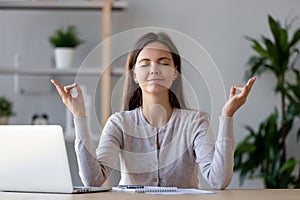 Calm young woman taking break doing yoga exercise at workplace