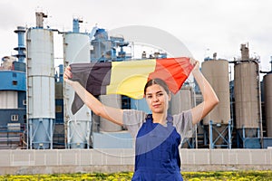 Calm young woman worker with flag of Belgium against background of factory