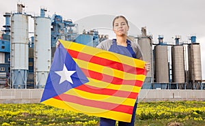 Calm young woman worker with flag of Catalonia against background of factory