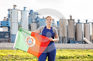 Calm young woman worker with flag of Portugal against background of factory