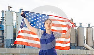 Calm young woman worker with flag of the USA against background of factory