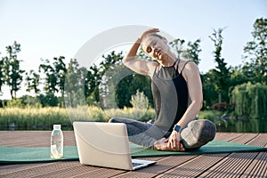 Calm your mind. Athletic beautiful middle aged woman watching instructional videos on a laptop while exercising on a mat