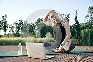 Calm your mind. Athletic beautiful middle aged woman watching instructional videos on a laptop while exercising on a mat photo