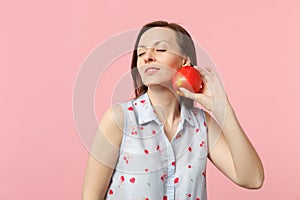 Calmed young woman in summer clothes keeeping eyes closed holding fresh ripe red apple fruit isolated on pink pastel