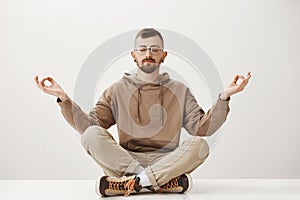 Calming down and uniting with nature. Confident relaxed young buddhist in stylish clothes sitting in urban park with