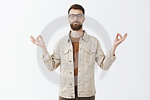 Calming down with yoga. Portrait of relieved peaceful good-looking urban guy in jacket with long sick beard closing eyes