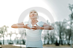 Calming elderly missis doing breathing exercises in the open air