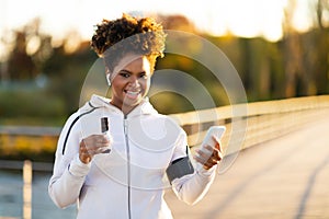 Calorie Counter App. Smiling Black Woman Using Smartphone And Eating Protein Bar