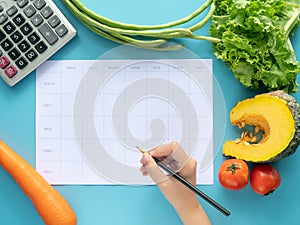 Calories control, meal plan, food diet and weight loss concept. top view of hand filling meal plan on blank paper with calculator