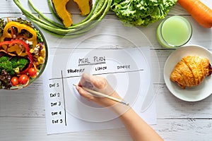 Calories control, meal plan, food diet and weight loss concept. top view of hand filling meal plan on weekly table with salad