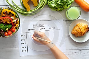 Calories control, meal plan, food diet and weight loss concept. top view of hand filling meal plan on weekly table with salad photo