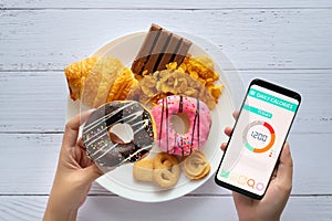 Calories counting and food control concept. woman using Calorie counter application on her smartphone with doughnut in hand photo