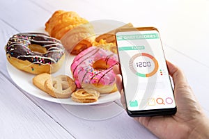 Calories counting and food control concept. woman using Calorie counter application on her smartphone with doughnut ,snack